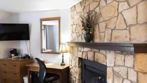 A room with a stone fireplace, a flat-screen TV mounted on the wall, a wooden desk, and a chair. - Schott’s Lake Conference & Resort (Sundre)