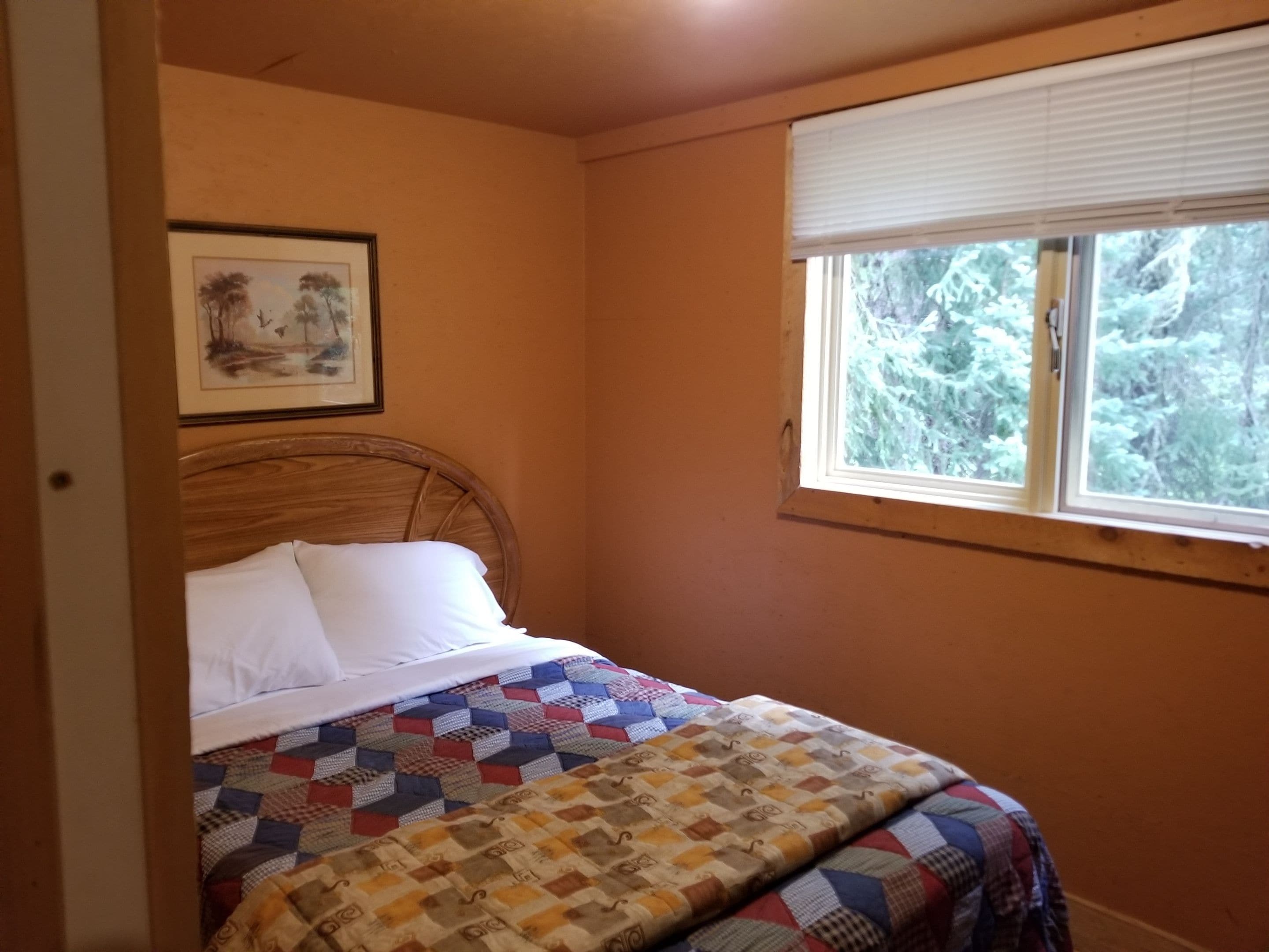 Ein Schlafzimmer mit einem Bett, einem Fenster mit Blick auf Bäume und einem Bild an der Wand.