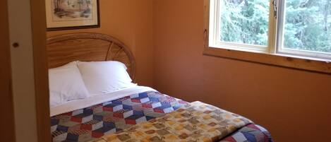Un dormitorio con una cama, un ventanal con vista a árboles y un cuadro en la pared.
