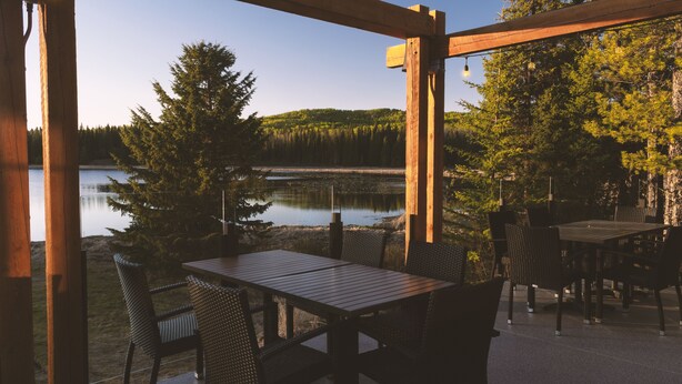 A wooden deck with a table and chairs overlooking a lake and forest. - Schott’s Lake Conference & Resort (Sundre)