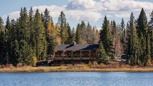 A lodge with a deck overlooking a lake, surrounded by dense forest. - Schott’s Lake Conference & Resort (Sundre)