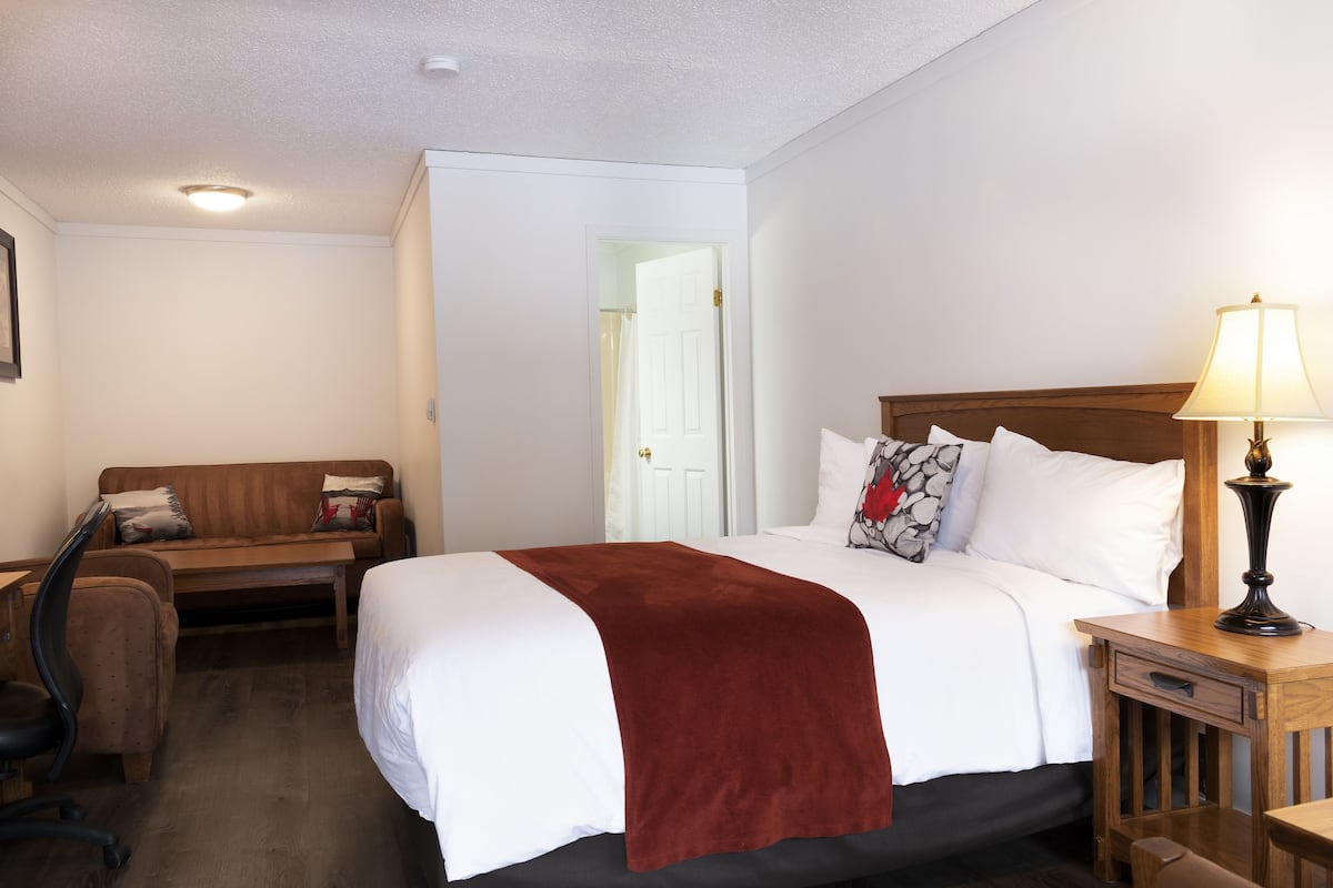 A hotel room with a bed, a desk, a chair, and a lamp.