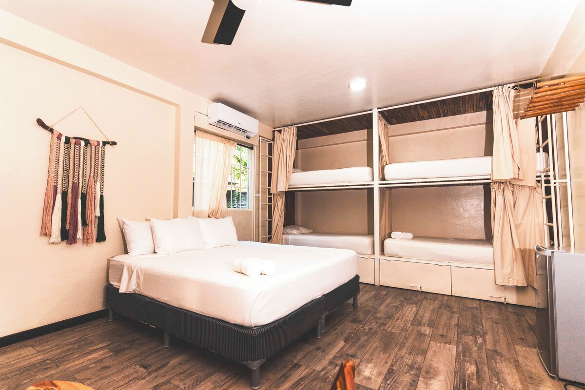 Une chambre avec un lit simple, un lit superposé, un plancher en bois et un climatiseur fixé au mur.
