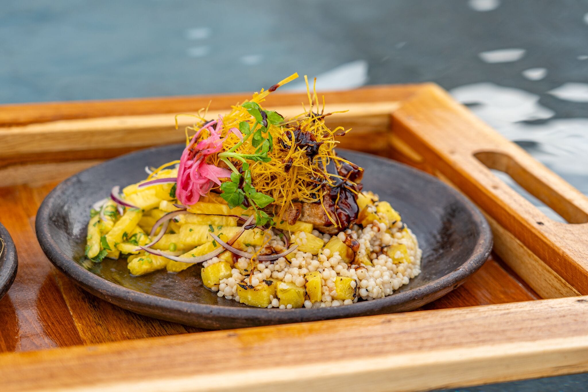 Un plato con piña a la parrilla, granos y guarniciones sobre un plato oscuro.