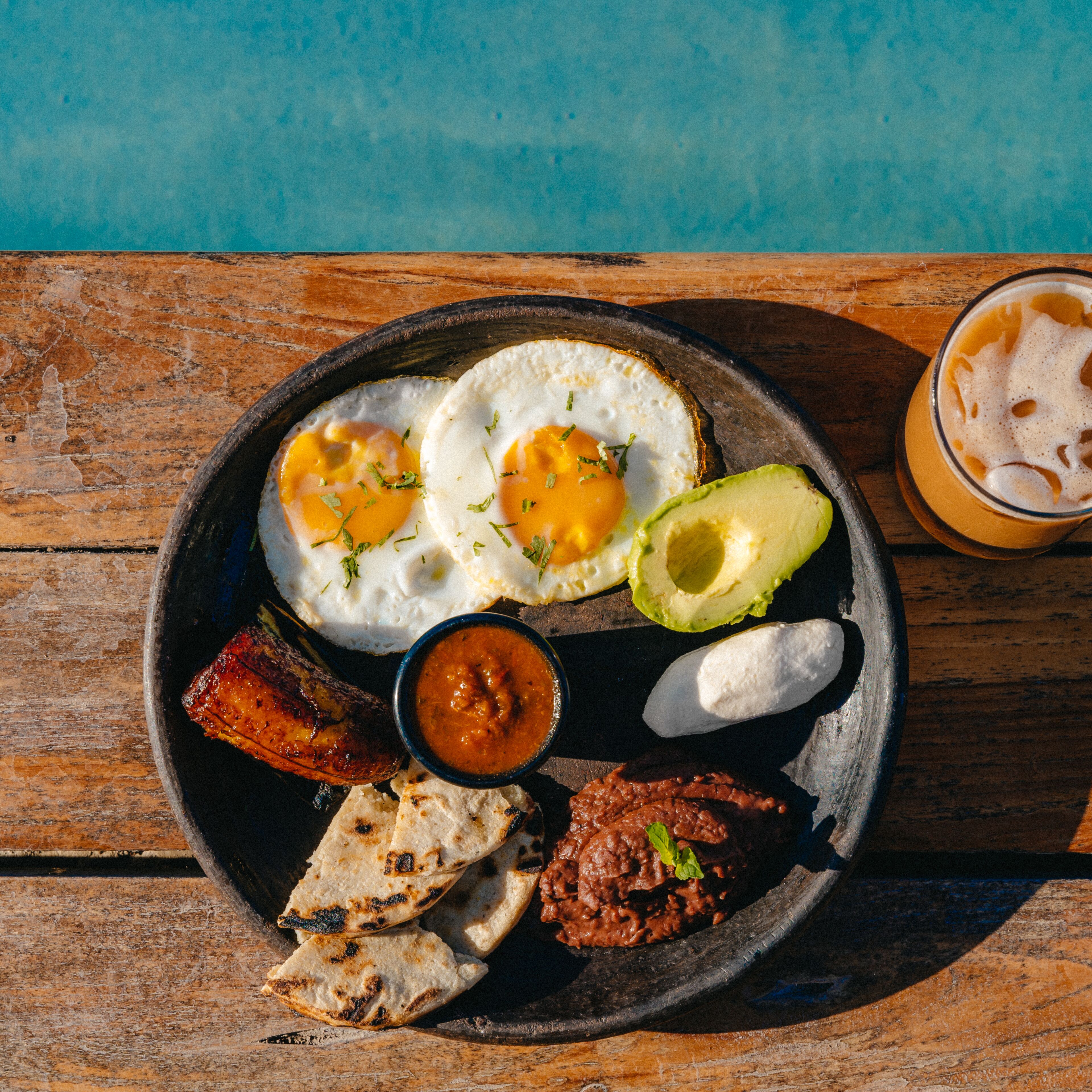 A plate of food including eggs, avocado, and various sides on a wooden table.