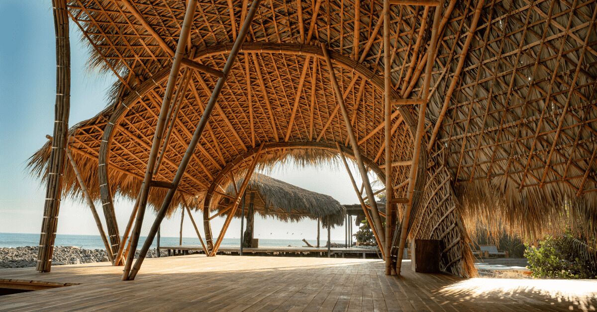 A wooden deck with thatched roof structures, a beach view, and a rocky shoreline.