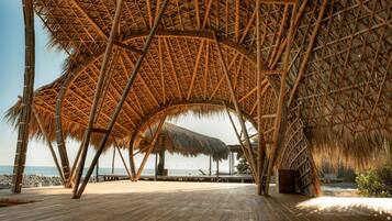 A wooden deck with thatched roof structures, a beach view, and a rocky shoreline.