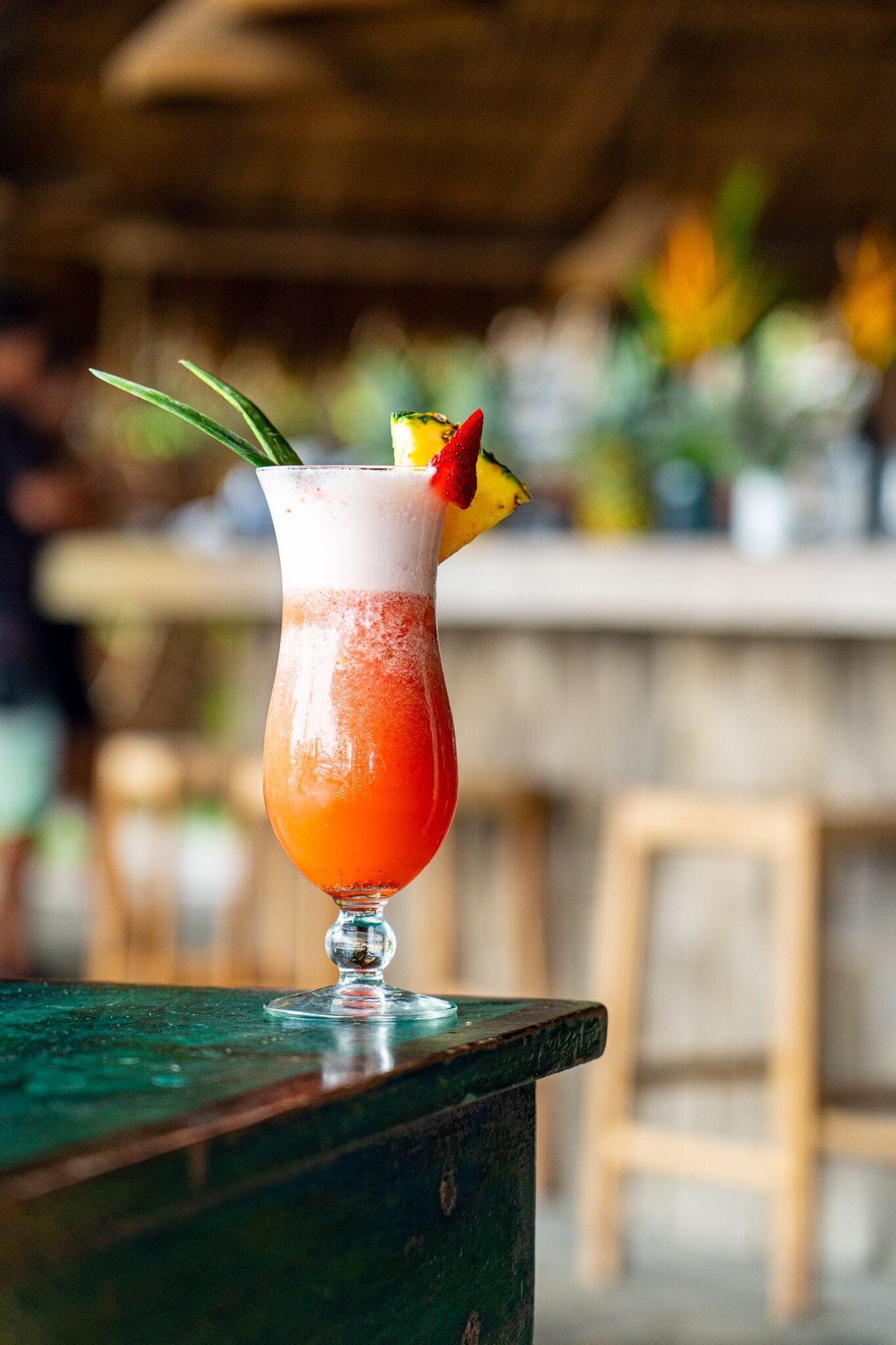 A cocktail in a glass with a straw and a slice of fruit on the rim, placed on a wooden table.