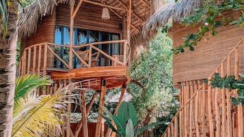 A thatched-roof wooden structure with a balcony, surrounded by lush greenery.
