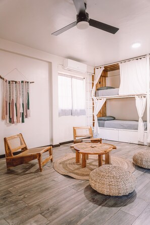 A room with a ceiling fan, bunk beds with white curtains, a woven chair, a woven table, and a woven pouf.