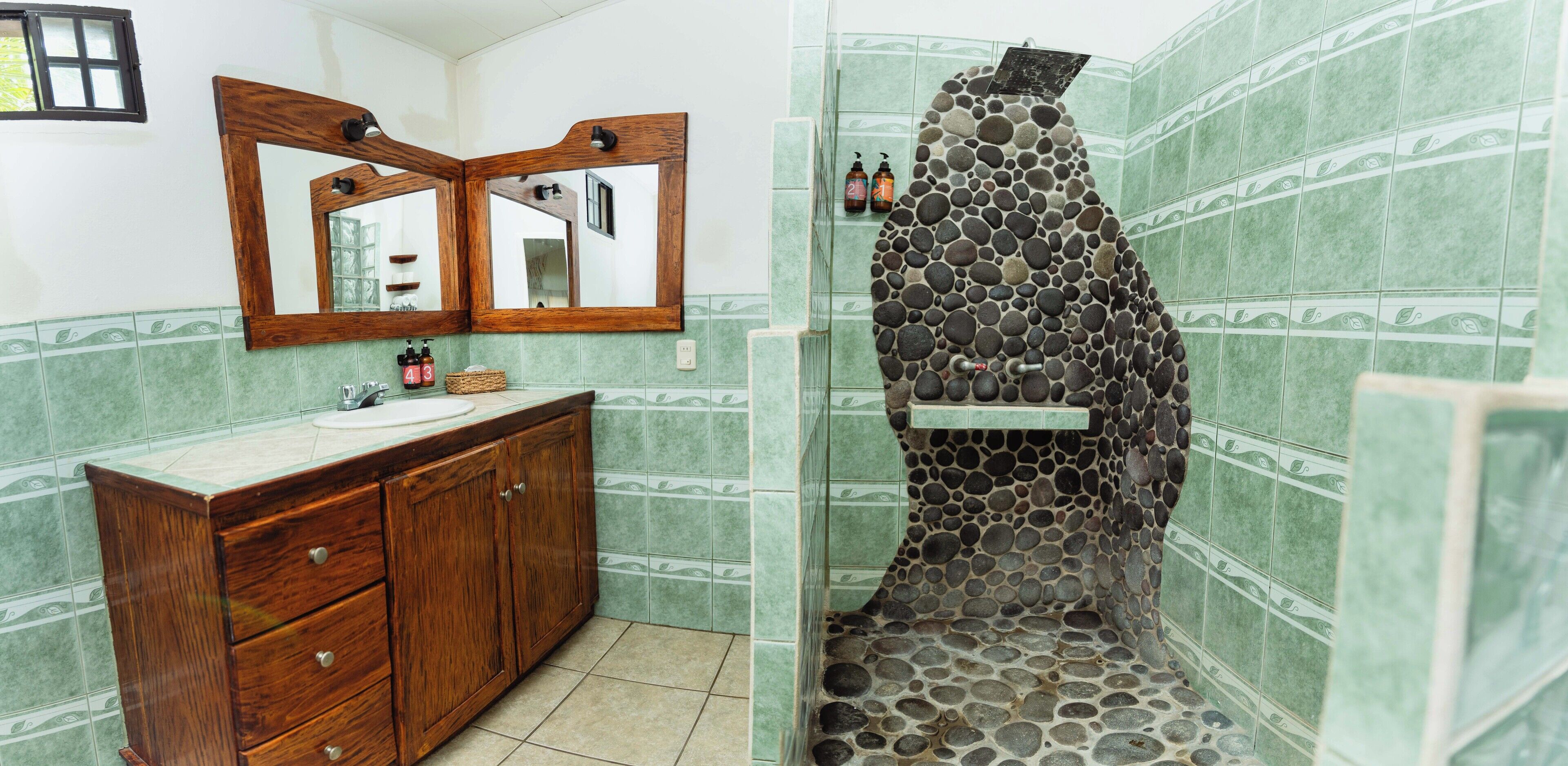 Une salle de bain avec un meuble-lavabo en bois, un grand miroir et une douche avec un mur en pierre.