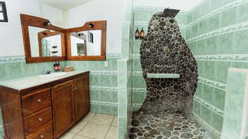 Une salle de bain avec un meuble-lavabo en bois, un grand miroir et une douche avec un mur en pierre.