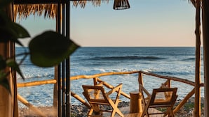 Una terraza de madera con dos sillas mirando al océano, un techo de paja y vista al mar.