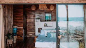 Una habitación con piso de madera, una cama, un ventanal grande y una lámpara colgante.