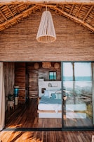 A room with a wooden floor, a bed, a large window, and a hanging light fixture.