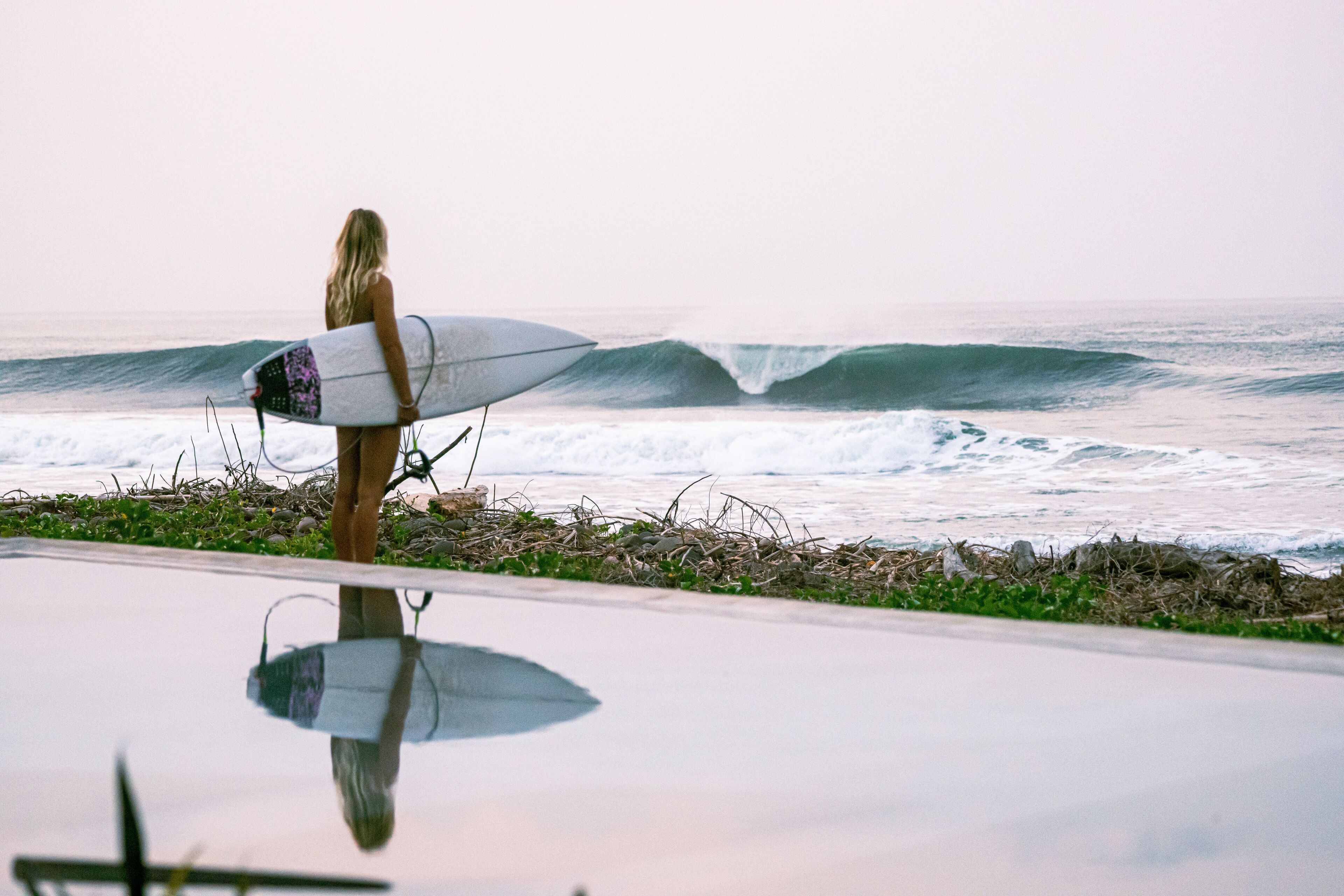 Iemand houdt een surfplank vast aan de kust.