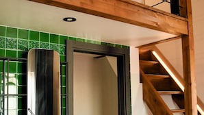 Ein Badezimmer mit einem weißen Waschbecken, grünen Fliesen, einem Spiegel und einer Holztreppe.