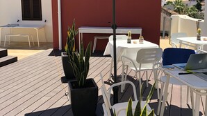 Eine Außenpatio mit Tisch und Stühlen unter einem großen Sonnenschirm, umgeben von Blumentöpfen.