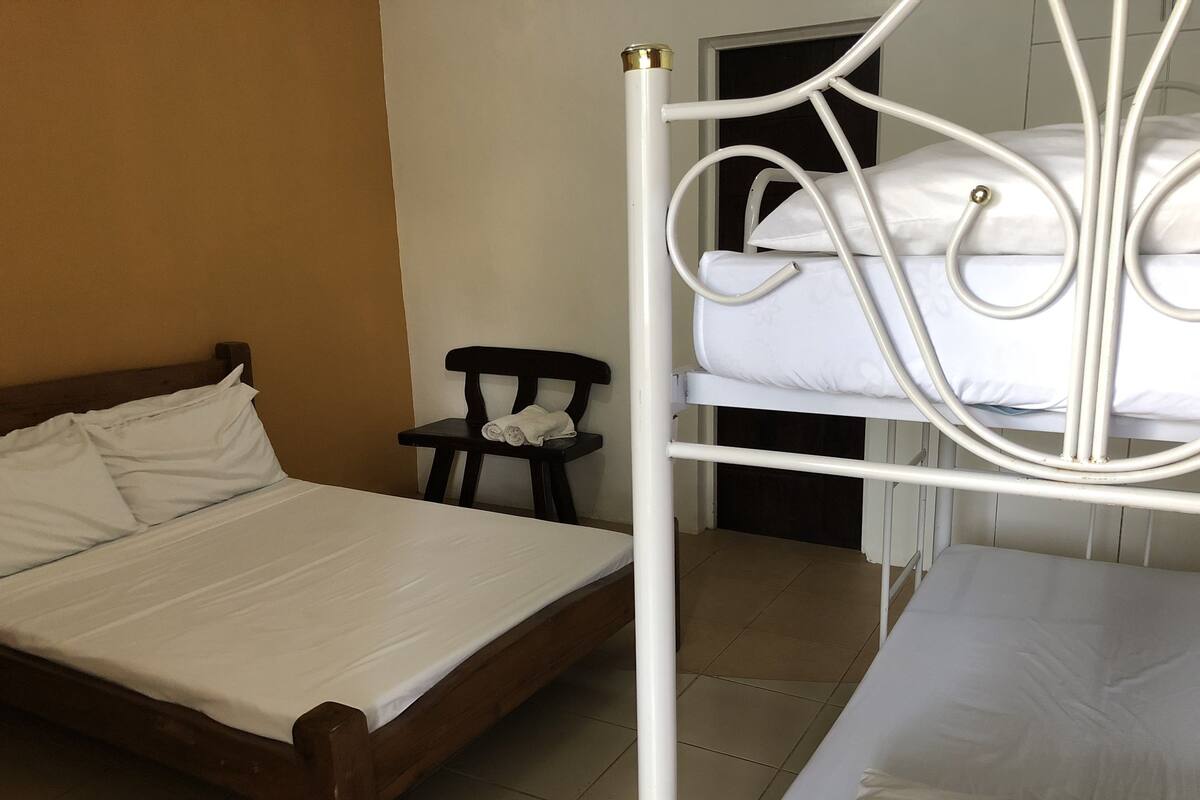 A room with a wooden bed, a small black chair, and a bunk bed with white bedding.