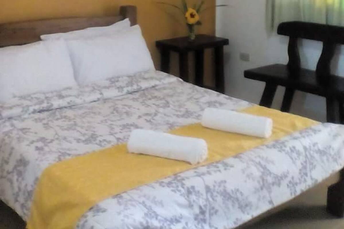 A hotel room with a bed, a small table with a vase of flowers, and a chair.