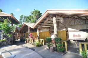 Une rangée de bâtiments de style traditionnel, avec des toits en tuiles et des piliers en bois, entourés de jardins aménagés et d’un chemin pavé.