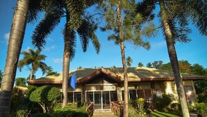 A two-story building with a sloped roof, surrounded by palm trees and other tropical vegetation. - Zacona Eco-Resort and Biblical Garden (San Pablo)