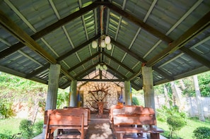 A covered outdoor seating area with wooden benches and a stone wall with a tree sculpture. - Zacona Eco-Resort and Biblical Garden (San Pablo)