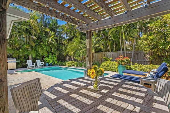 A backyard with a pool, wooden pergola, lounge chairs, and a grill.