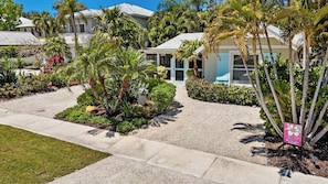 A residential area with a paved driveway, palm trees, and a house with a white exterior.