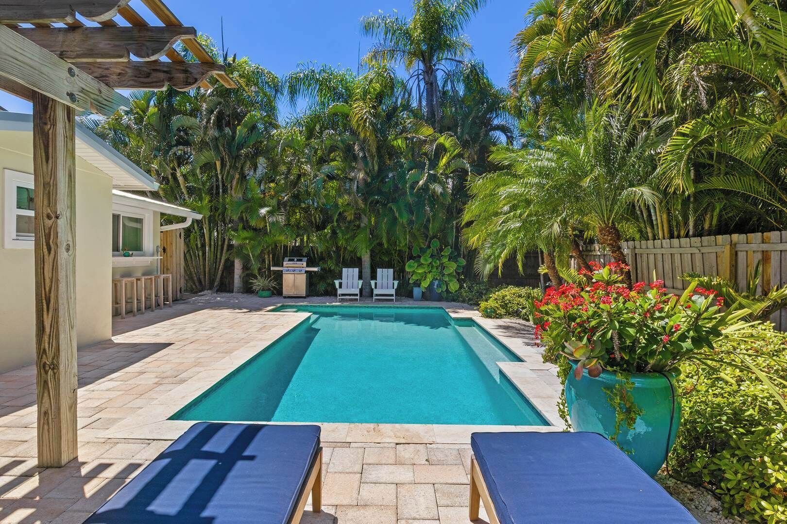 Une piscine rectangulaire agrémentée d’une pergola en bois et de chaises longues.