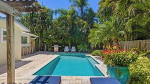 Una piscina rectangular con un pérgola de madera y sillas de descanso.
