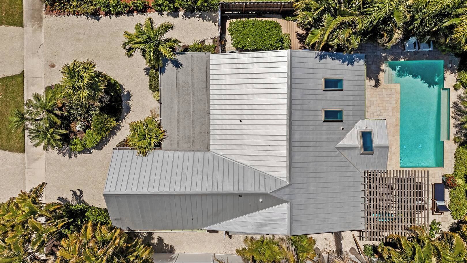 An aerial view of a modern building with a swimming pool, surrounded by palm trees and a wooden deck.