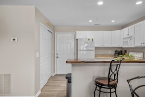 Una cocina con armarios blancos, encimera de madera, refrigerador y microondas.