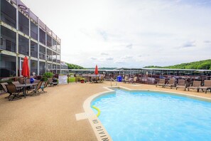 A pool area with lounge chairs, a dining table, and a building with multiple balconies.
