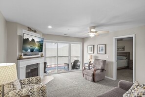 Una sala de estar con chimenea, televisor, ventilador de techo y un balcón con mobiliario exterior.