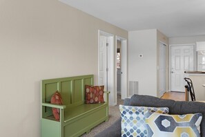 A living room with a green sofa, a grey sofa, and a kitchen area in the background.