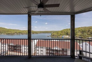 A balcony with a view of a lake, buildings in the background, and a ceiling fan.