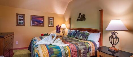 A neatly made bed with a colorful quilt, two bedside lamps, and a wooden nightstand.