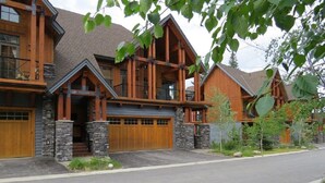 A large, multi-story log cabin with a prominent front porch, stone pillars, and a garage. -  Ski-In Ski-Out, Private Hot Tub, Spacious End Unit, Panoramic View (Golden)