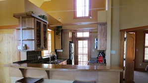 A kitchen with a central island, two bar stools, wooden cabinets, a refrigerator, and a window with blinds. -  Ski-In Ski-Out, Private Hot Tub, Spacious End Unit, Panoramic View (Golden)