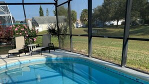 A clear swimming pool with a tiled edge, surrounded by a covered patio area with chairs and a table. - Last-minute special, NEW beds/AC/pool heater/laminate floor, park view! (Kissimmee)