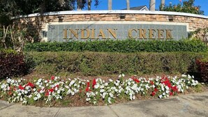A sign for Indian Creek with a stone wall and flower beds in front. - Last-minute special, NEW beds/AC/pool heater/laminate floor, park view! (Kissimmee)