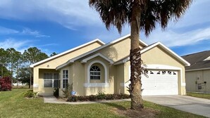 A single-story house with a garage, a front yard with grass and a palm tree, and a clear sky. - Last-minute special, NEW beds/AC/pool heater/laminate floor, park view! (Kissimmee)