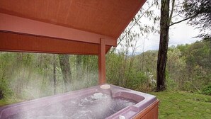 Un bain à remous sous une pergola en bois, avec vue sur une zone boisée.