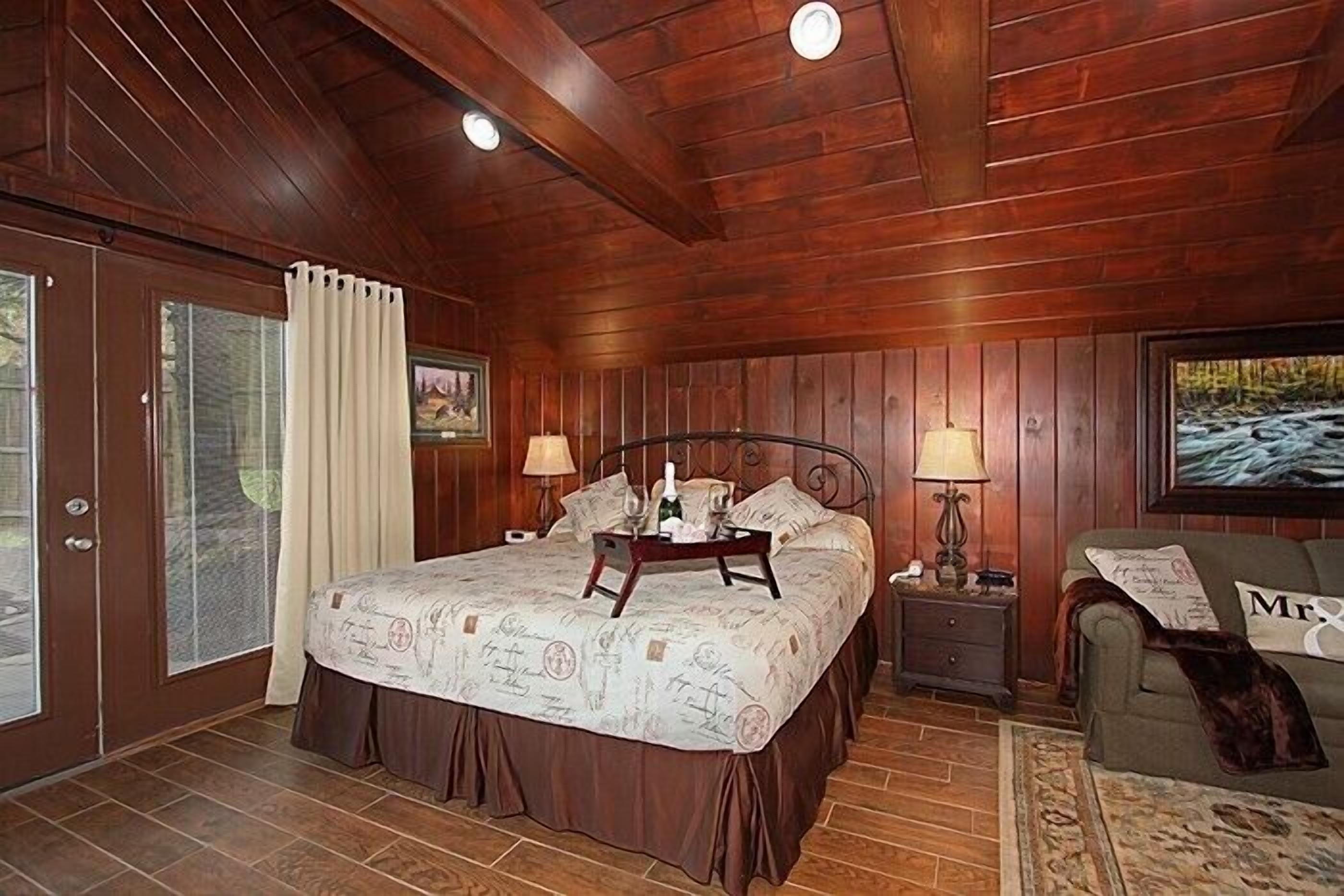 Un dormitorio con paneles de madera, una cama, mesitas de noche y un sillón verde.