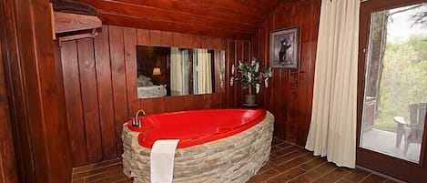 Une salle de bain rustique, avec des murs en bois, une baignoire en pierre, un miroir et une fenêtre agrémentée de rideaux.