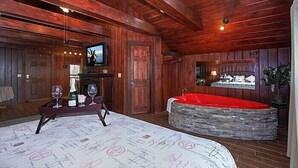 L’intérieur d’un chalet en bois comprend une baignoire en pierre, un téléviseur et une table à manger avec des verres à vin.