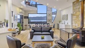A modern living room with a large window, a stone fireplace, and a dining area with a view of the mountains. - Quarry Hill Lookout ..... scenic views, luxurious amenities, relaxing atmosphere (Huon Valley)