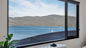 A room with a large window overlooking a body of water and hills. - Quarry Hill Lookout ..... scenic views, luxurious amenities, relaxing atmosphere (Huon Valley)