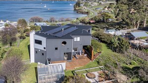 A modern house with a large deck, solar panels, and a view of a lake and hills. - Quarry Hill Lookout ..... scenic views, luxurious amenities, relaxing atmosphere (Huon Valley)